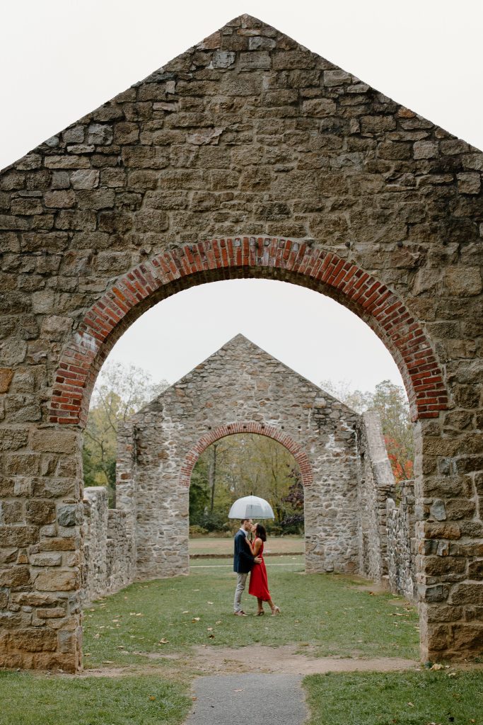 man and woman under umbrella kissing under stone arch