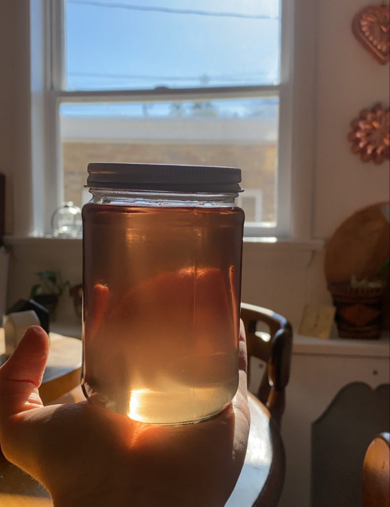 picture of my hand holding lavender simple syrup in the sunlight in a jar