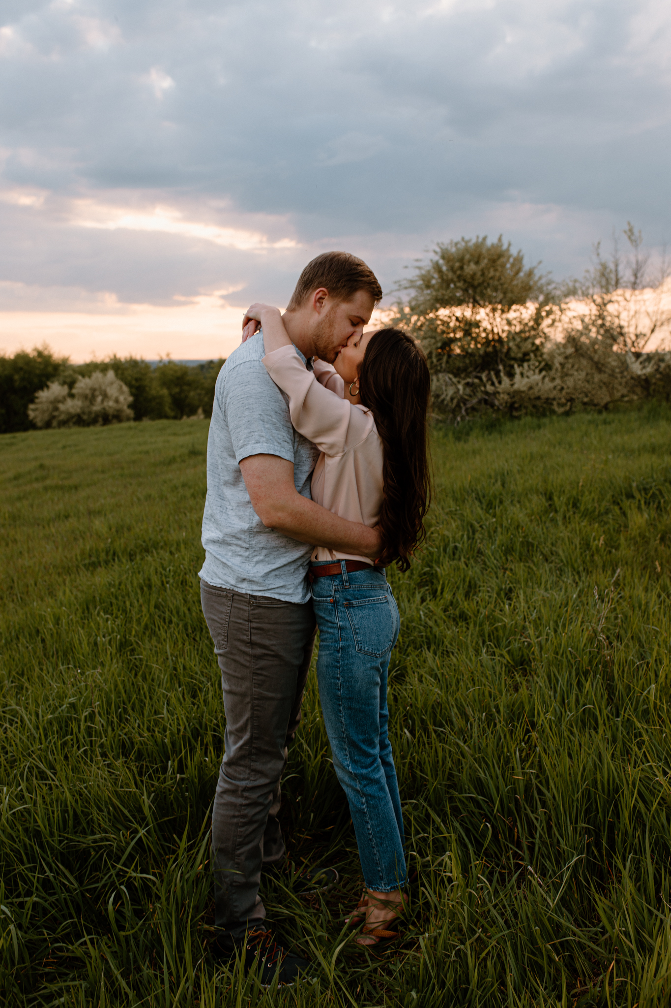 couple kissing in a field with the pink sunset in the background